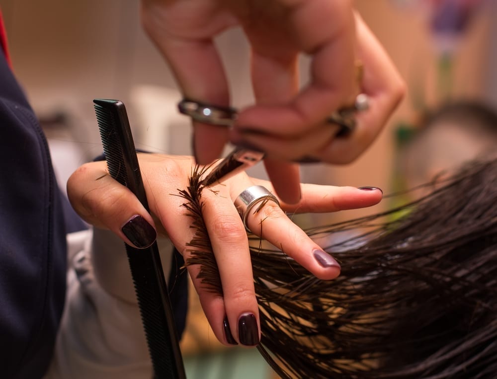 Professional stylist trims a woman's brown hair.
