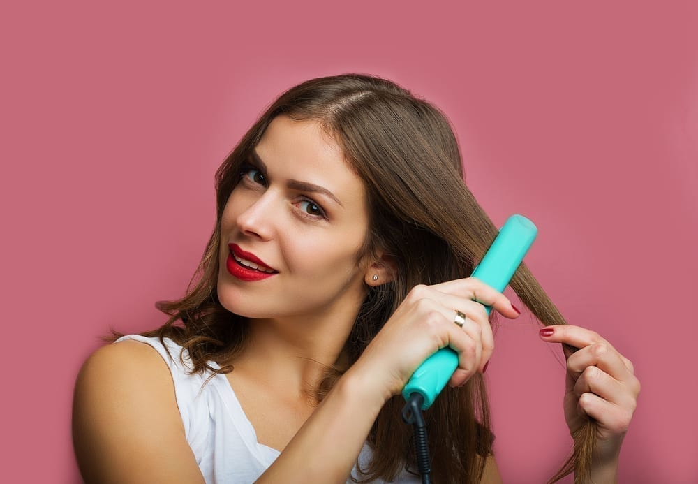 Girl with long dark hair uses a straightening iron. 